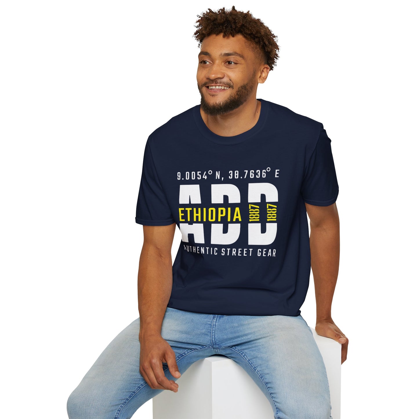 Man wearing a navy blue t-shirt with Addis Ababa, Ethiopia, ADD Airport code and coordinates, sitting on a white stool against a white background.