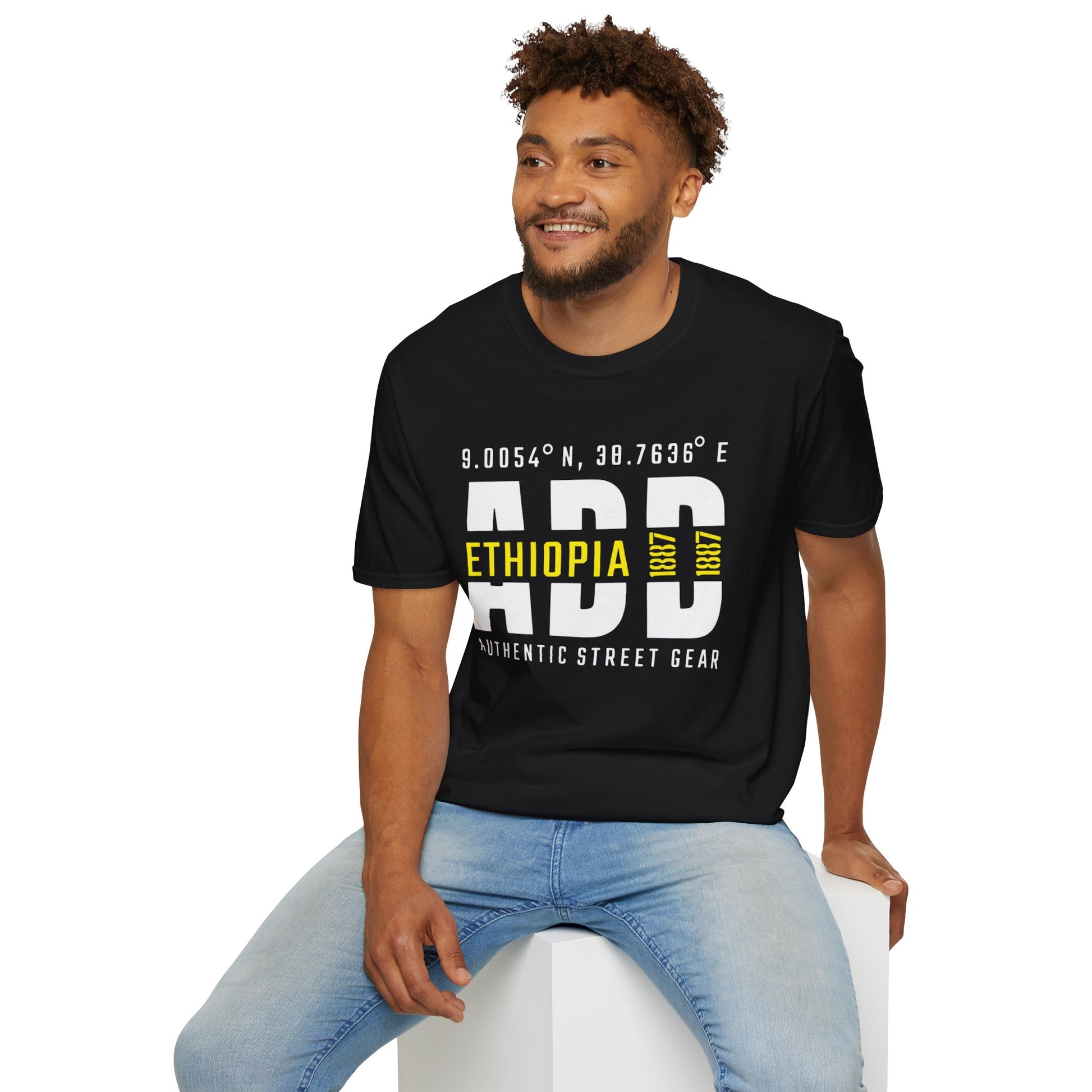 Man wearing a black t-shirt with Addis Ababa, Ethiopia, ADD Airport code and coordinates, sitting on a white stool against a white background.