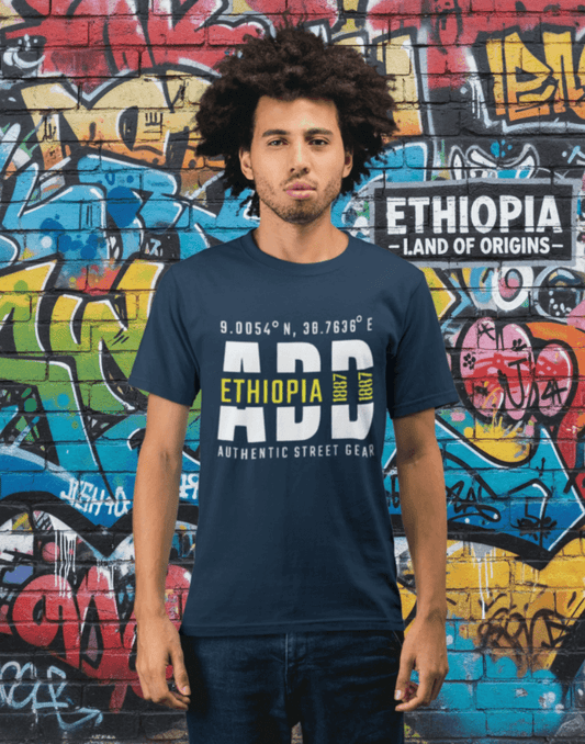 Man wearing a blue t-shirt with Addis Ababa, Ethiopia, ADD Airport code and coordinates standing before a graffiti wall background