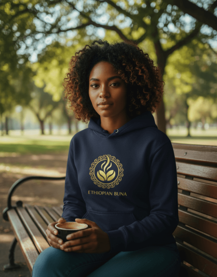 Woman wearing a navy blue Ethiopian Buna graphic print hoodie holding a cup of coffee in a cozy setting