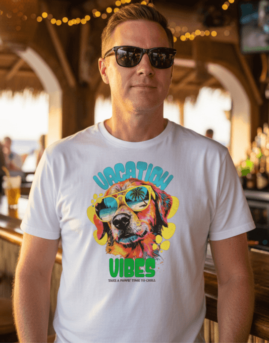 Man with a white t-shirt with a dog wearing sunglasses and text that says Vacation Vibes Take a Paws! Time to chill. Man is standing at a bar