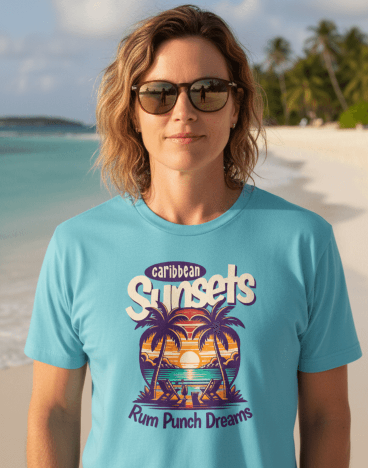 Woman on the beach wearing a sky blue t-shirt that says Caribbean Sunsets, Rum Punch Dreams with a beach sunset graphic.