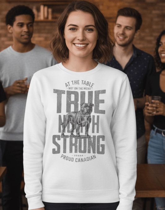 Woman wearing a white sweatshirt with text and graphics, True North Strong, standing indoors with people in the background.