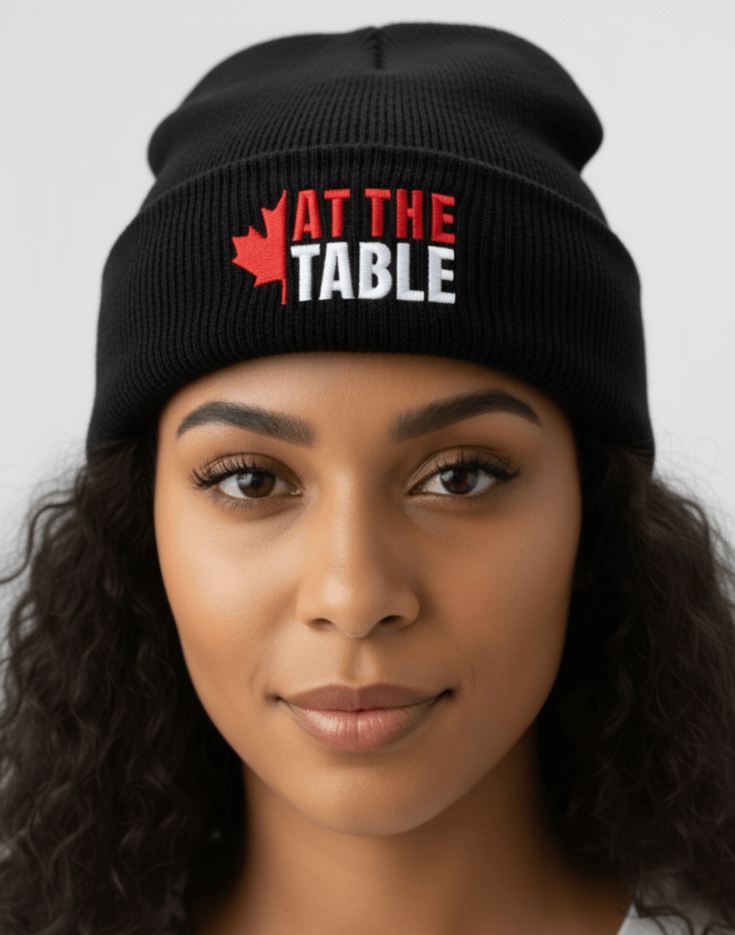 Black beanie with 'AT THE TABLE' logo worn by a person against a neutral background