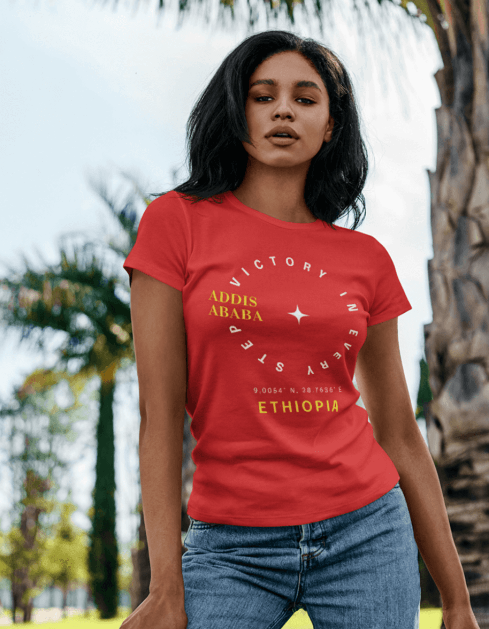 Woman wearing a red Ethiopian, Addis Ababa, minimalist, t-shirt with yellow and white text, standing outdoors with trees in the background
