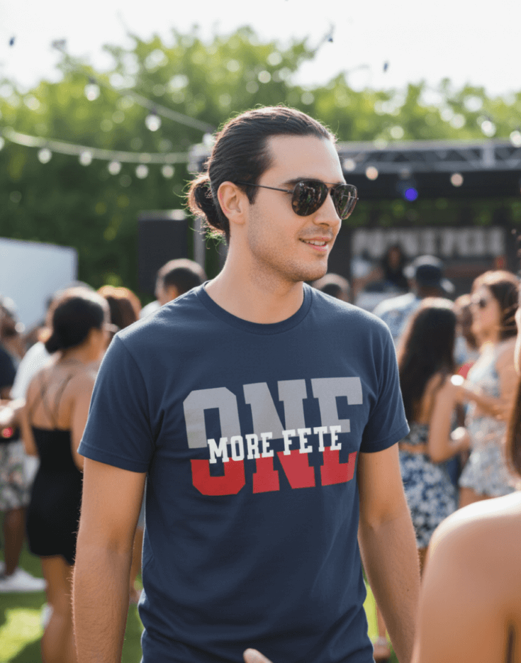 Man wearing sunglasses and a navy t-shirt with 'ONE MORE FETE' text at an outdoor event.