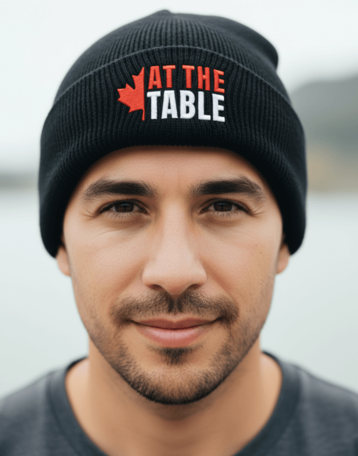 Man wearing a black beanie with 'At The Table' logo, blurred background