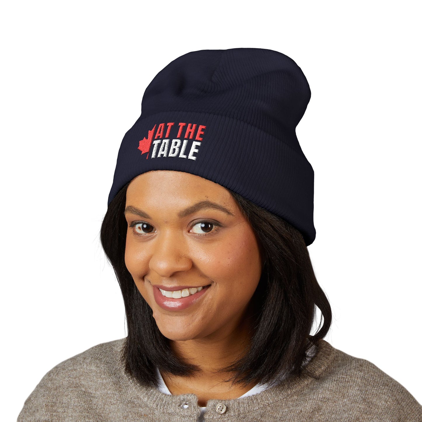 Person wearing a navy beanie with 'At the Table' text and maple leaf graphic on a white background